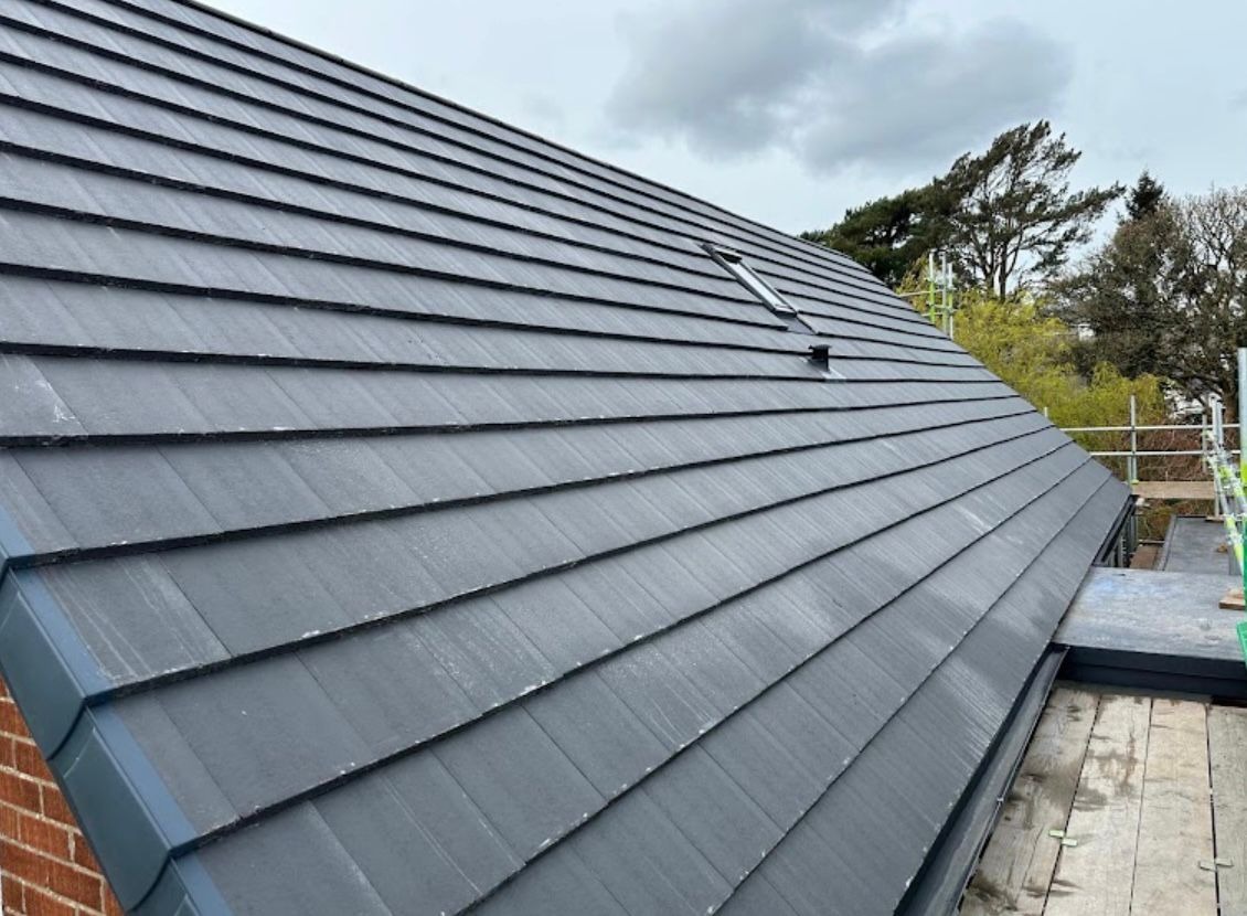 Newly completed grey flat-profile tiled pitched roof with velux window after a full re-roof