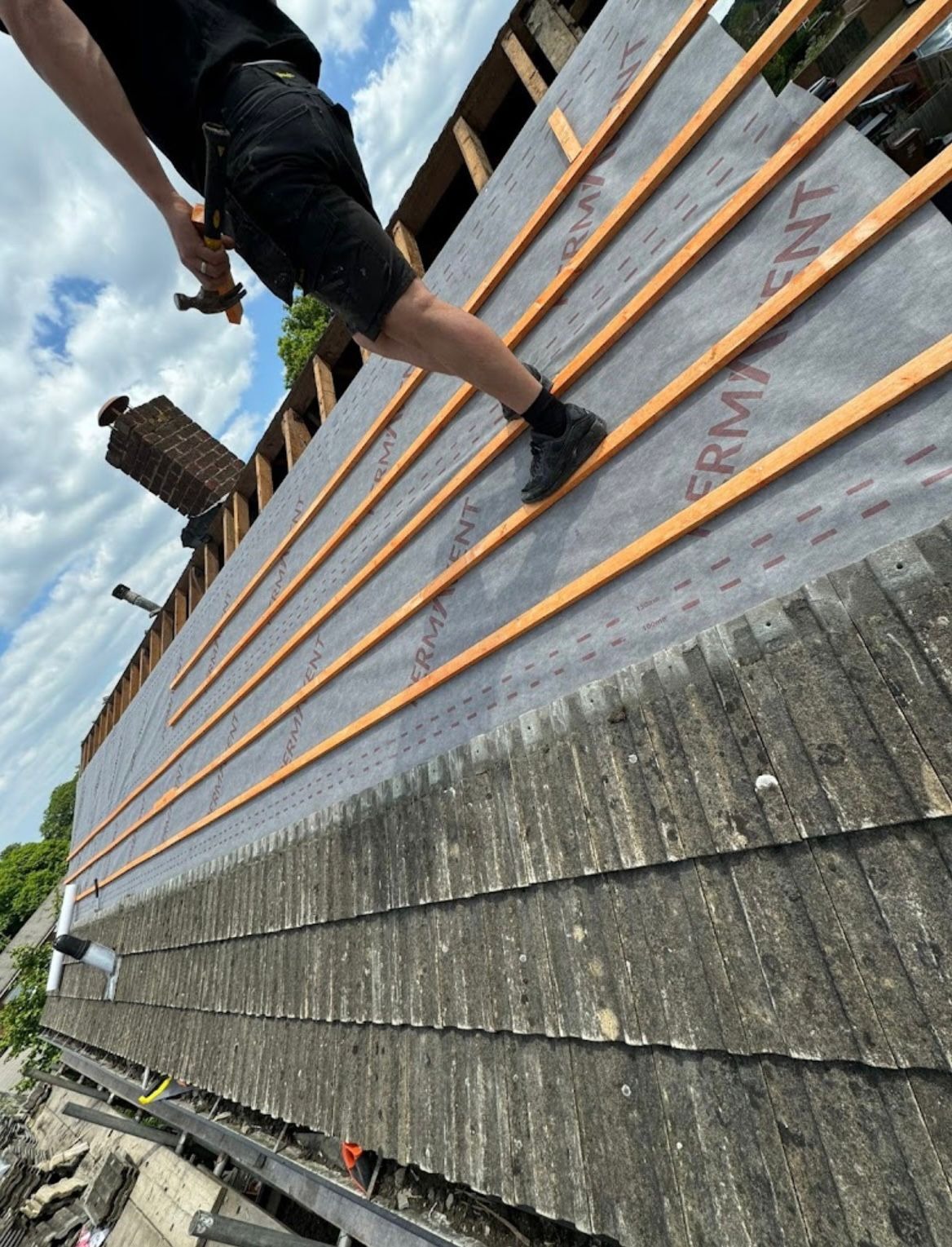 Roofer fixing treated battens over breathable membrane during a pitched roof strip and re-roof